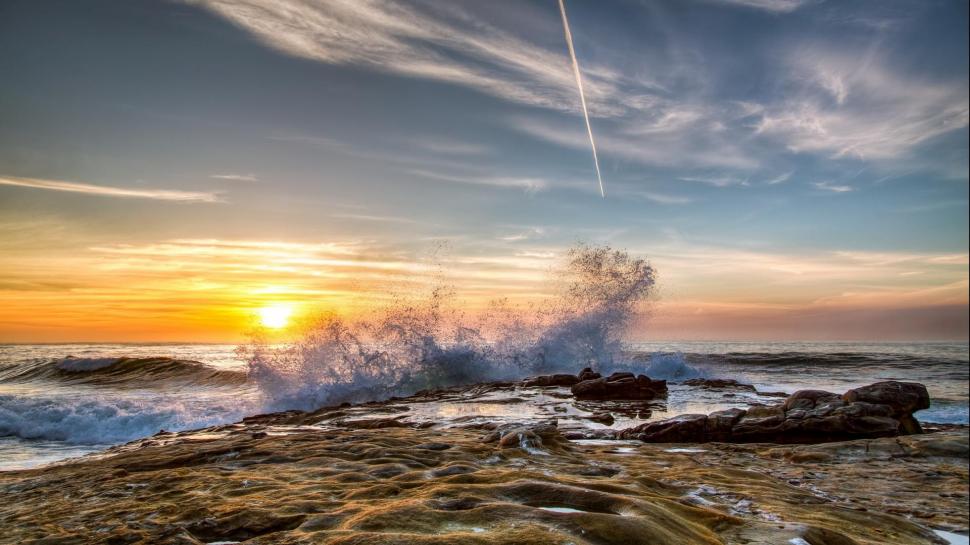 Wave Breaking On Rocky Shore At Sunset wallpaper,shore HD wallpaper,rocks HD wallpaper,wave HD wallpaper,plane trail HD wallpaper,sunset HD wallpaper,nature & landscapes HD wallpaper,1920x1080 wallpaper